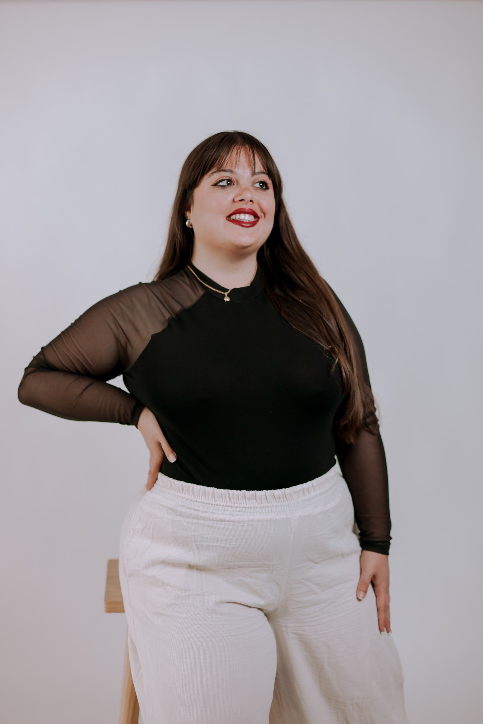 Retrato de Adriana May sonriendo, con top negro de mangas transparentes, sobre fondo claro